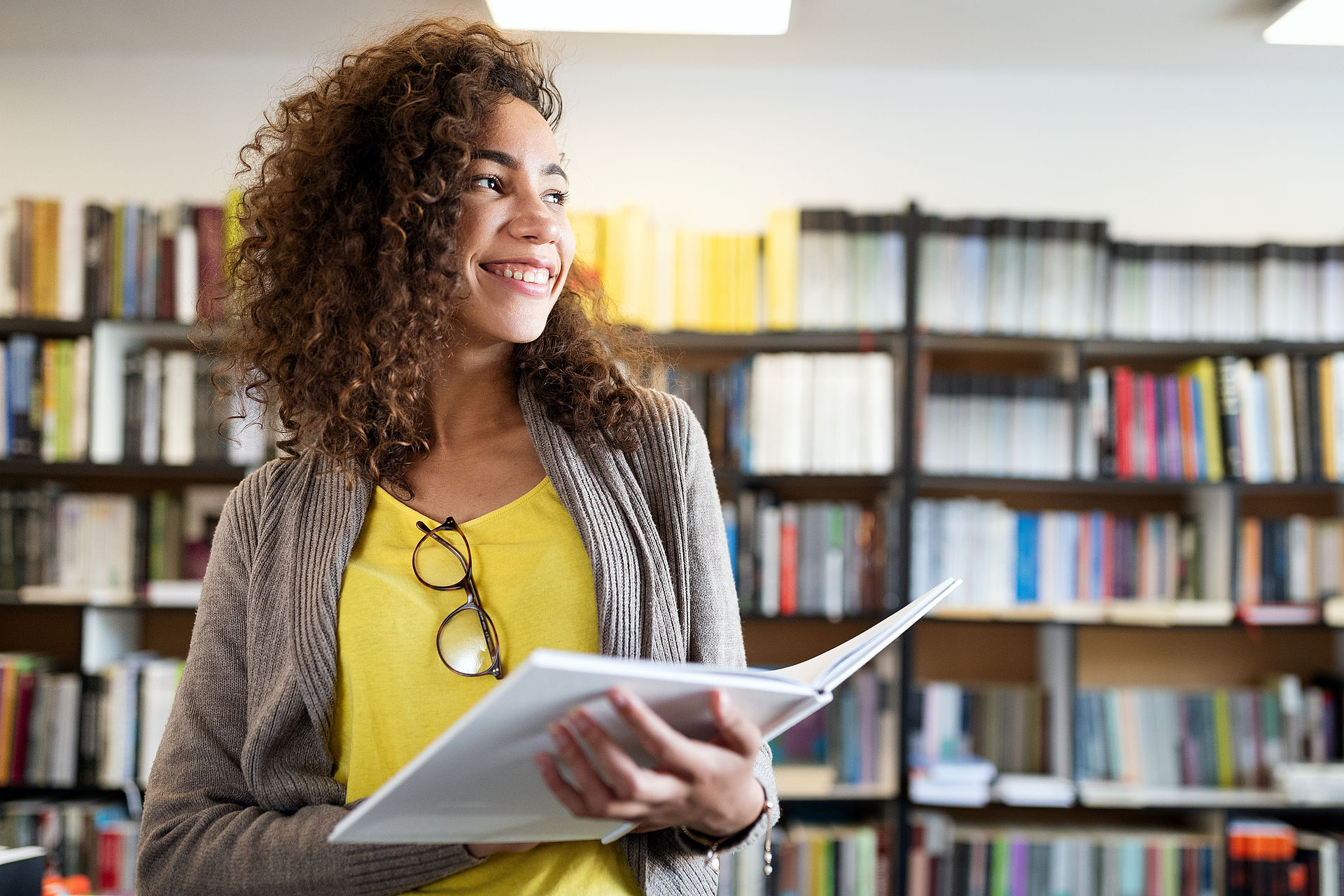 Junge lächelnde Frau in Bibliothek mit Buch in der Hand