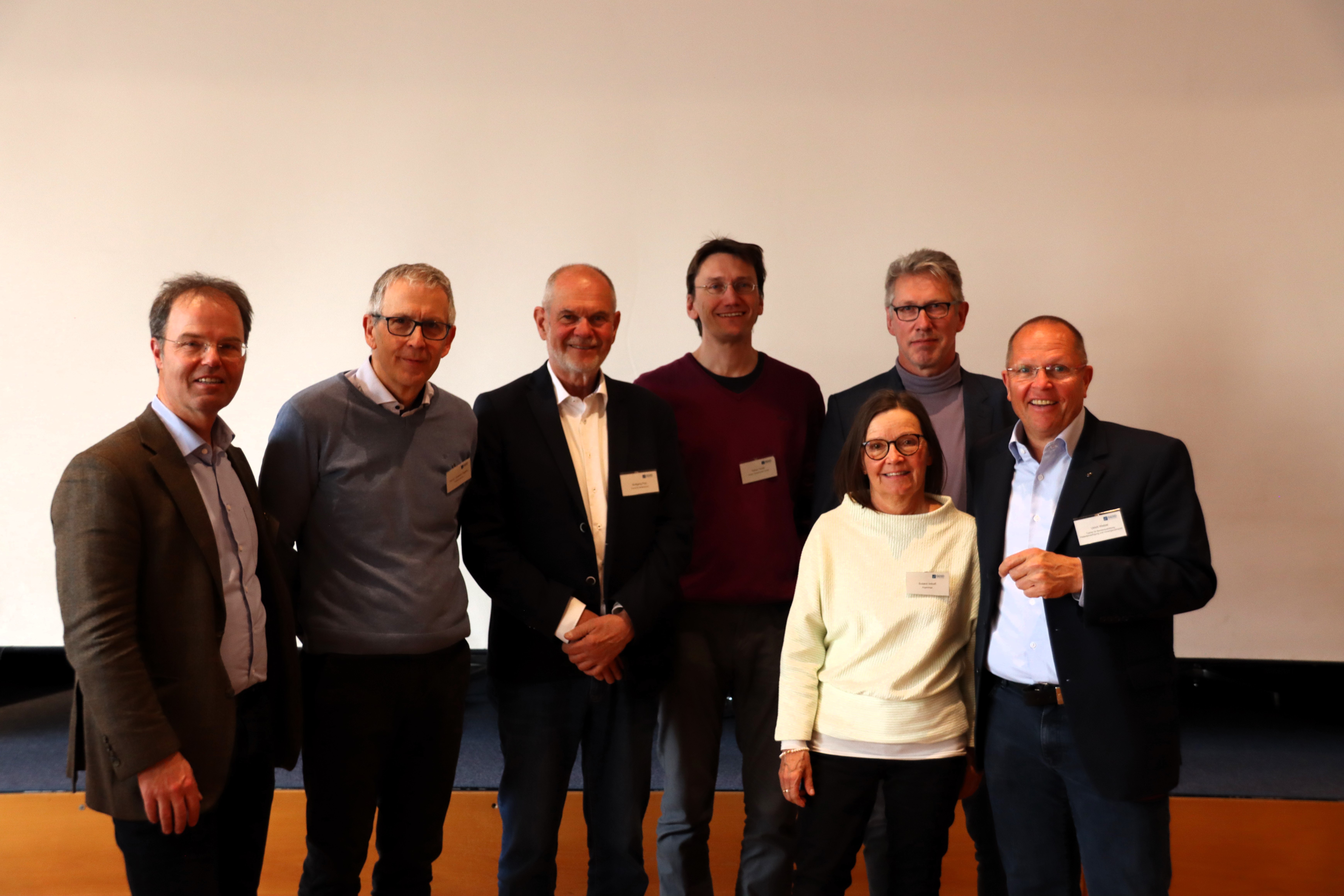 Gruppe von sieben Menschen lächelt freundlich in Kamera